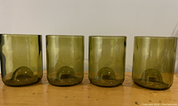 Side view of four green glasses made from recycled wine bottle bottoms, showing their consistent height and shape.