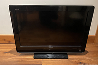Front view of black Sony Bravia 30-inch TV with a glossy bezel and stand shown on wooden floor.