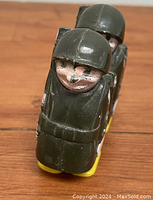 Front view of two green plastic toy soldiers connected side by side, showing detailed helmets and painted faces.