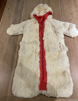 Front view of baby-size fur snug coat. Light cream-colored fur exterior with an attached hood. Red fabric lining visible through front opening and a zipper closure.