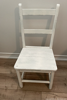 Front view of white wooden chair showing the seat and ladder back design.