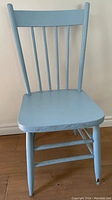 Front view of a blue painted wooden chair with four vertical slats on the backrest, showing wear on the seat and legs.