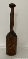 Wooden mallet standing upright against a white wall showing the full length and handle detail.