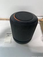 Front angled view of the black Amazon Echo Studio speaker showing fabric covering and top control buttons with an orange lit ring.