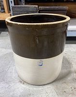 Side view of large antique stoneware crock with brown upper glaze and white lower half, stamped with number 6 in blue.