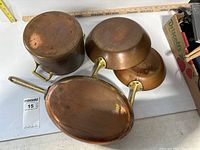 Top view of the 4 copper pots showing their shape and handles, arranged with interiors down.