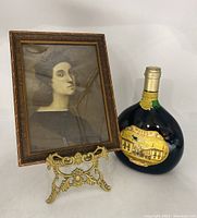 Framed portrait on the brass picture easel beside a vintage wine bottle