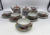 Front view of entire tea set laid out, showing five cups on saucers, teapot, sugar bowl and creamer