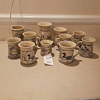 Nine Cornish pottery pieces including mugs and a vase with animal motifs in beige and black glaze with accents of blue and red.