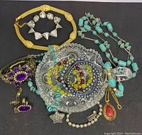 Top view of assorted modern costume jewelry including bracelets, necklaces, brooch, and earrings displayed in a cut glass dish.