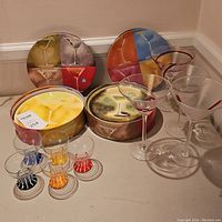 Angle showing complete set of round cocktail plate boxes, small colored stemmed glasses, and large cocktail glasses