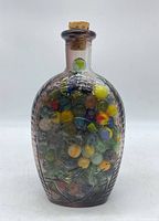 Front view of the amethyst colored glass Presidents jar filled with multicolored marbles and sealed with a cork.