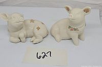 Two Lenox pig figurines together, one seated and one lying down, showing their floral decorations and jeweled accents.