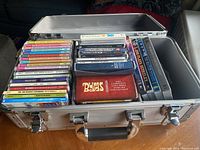 Image of metal carrying case filled with various CDs and DVDs including colorful box sets and individual titles.
