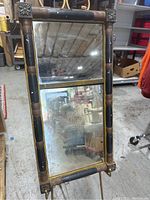 Front view of rectangular wall mirror with original glass showing signs of age and oxidation. Dark wood frame with gold accents and floral corner details. Brass dividing strip between two mirror sections.