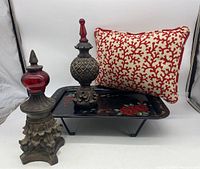 Photo showing the gray metal tray with legs, red and white pillow, and two decorative finials with carved details and painted finishes.
