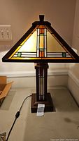 Front view of the lamp showing the stained glass pyramid-shaped shade and pull chain switch on the wooden base