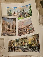 Five unframed art prints laid out on floor showing different scenes including architecture and crowds.