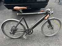 Side profile showing entire Wing electric bike, black frame with brown leather saddle and grips, disc brakes, standard wheels.