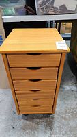 Front view of wood filing cabinet showing six drawers and wheels at base.