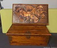 Front view of wooden box with open carved lid showing horse design and copper rivet accents on corners.