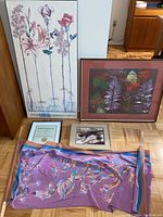 Two framed botanical art prints and smaller framed photograph arranged on floor beside folded fabric banner with bird and flower designs