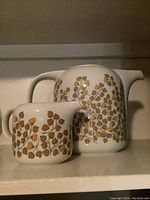 Front view of teapot and creamer showing gold leaf pattern and their handles and spouts.