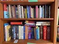 Two rows of assorted hardcover and softcover books arranged on a bookshelf with a variety of titles visible including dictionaries, finance books, and novels.