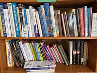 Books arranged on two wooden shelves with a mix of hardcover and softcover editions, showing titles and varying sizes.