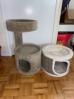 Two cat playhouses shown side by side; left is carpeted tunnel with top perch, right is round plush top cat house.