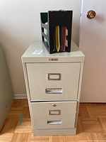 Full view of beige two-drawer metal filing cabinet with a black file folder organizer holding colored folders on top.