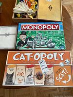 Boxes of Monopoly and Cat-Opoly board games with stationery set box next to them