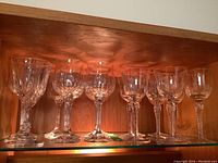 Seventeen glass wine glasses in three different patterns on wooden shelf with warm lighting, showing arrangement and glass details
