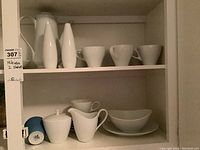 Shelved Mikasa white fine china including coffee pot, cups, saucers, bowls, platters and salt & pepper shakers.