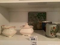 Shelf view showing cream and sugar set, two ceramic mugs, and artisan plate in background