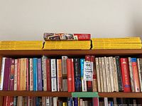 Bookshelf containing yellow-spined National Geographic magazines on top with various paperback novels arranged below.