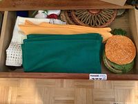 Drawer with folded green and orange fabric table mats, small decorative woven pumpkin container, and white towel.