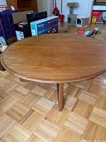 Round teak coffee table close-up showing natural wood grain and surface scratches.