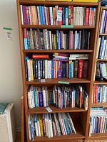 Teak veneer bookcase filled with assorted books, showing full frontal view.