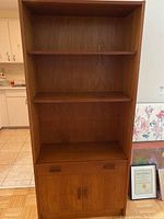 Full front view of a tall teak veneer cabinet with two shelves, a drawer area with handles, and lower cupboard doors.