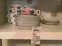 Stack of eight porcelain soup bowls with pink floral and green leaf design, each with two circular handles, and eleven saucers including eight matching and three mismatched ones.