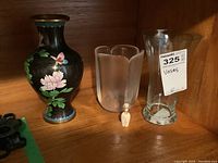 Shelved four vases: cloisonné, frosted glass, clear glass, and small cork vessel, all shown in a wooden cabinet.