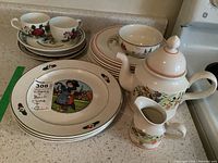 Photo showing the Villeroy & Boch Bon Appetit pattern teapot, creamer, salad plates, and dinner plates with folk art style illustrations.