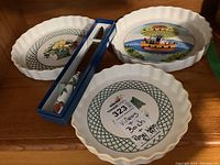 Photo showing three Villeroy & Boch ceramic pie plates, two with floral/lattice designs and one with boat scene, plus boxed Royal Worcester cake knife