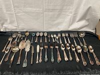 Wide photo of all silverware pieces laid out on dark cloth, showing variety and quantity