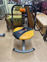 Front view of Ab Doer Twist exercise machine showing padded yellow and black seat, handlebars with foam grips, and metal frame.