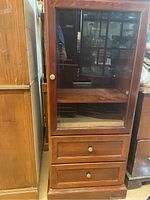 Front view of wooden Bombay cabinet showing glass door, internal shelf, and two drawers.