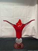 Front view of large red blown glass vase with extended arms and clear textured base on black fabric and white background.