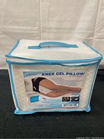 Photo of the knee gel pillow in its original packaging case with handle. The packaging shows the product name, image of pillow use on a side sleeper, and product features.