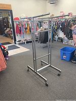 Full view of the adjustable metal clothing rack showing angled side with two horizontal adjustable arms and four wheels.